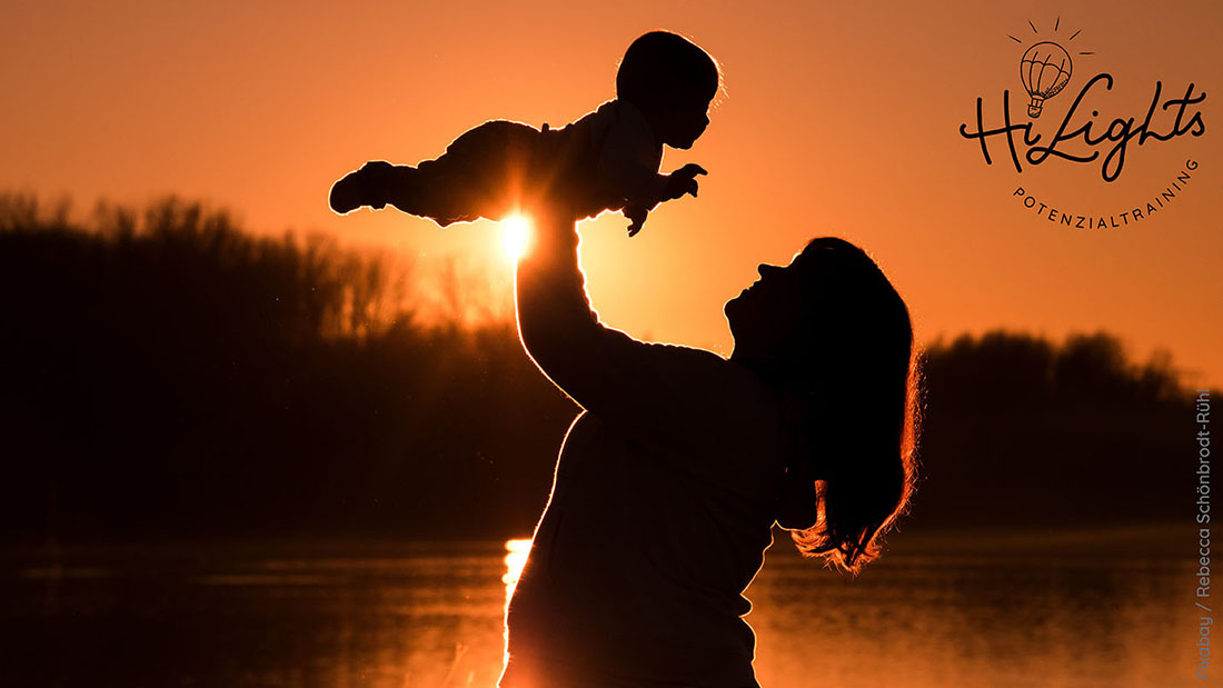 Mutter haelt KInd nach oben im Hintergrund Sonnenuntergang - 50